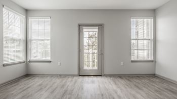 A room with plank flooring and a large window with blinds.